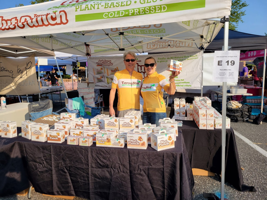 A lively farmers market scene featuring a diverse group of people selecting colorful, plant-based snacks from a rustic wooden stall.