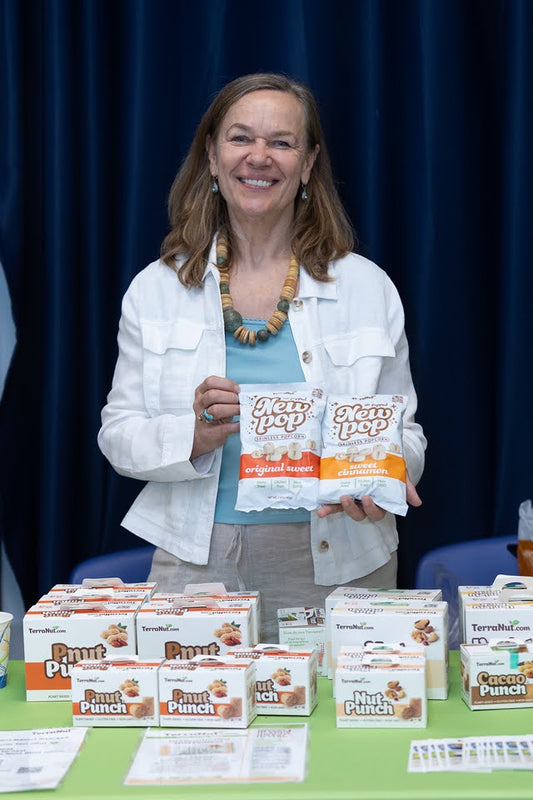 TerraNut founder Urszula holding bags of NEW POP skinless popcorn behind a trade show product display.