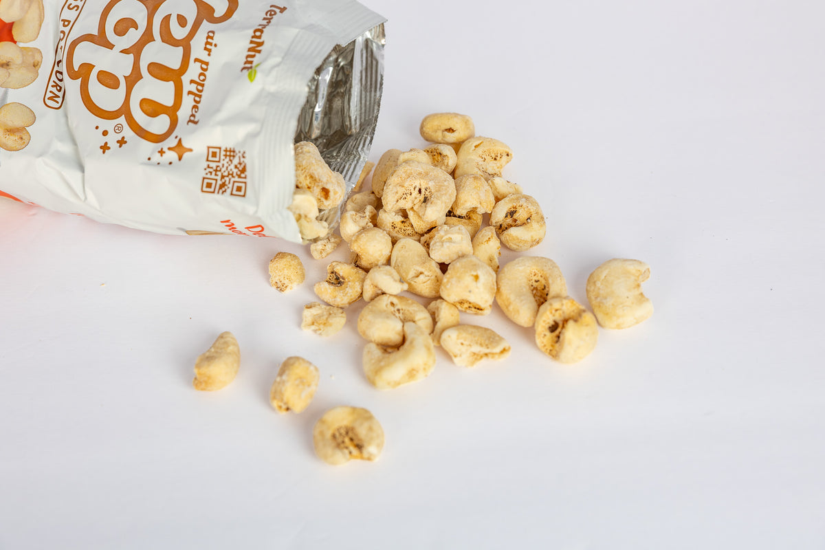 Open bag of TerraNut New Pop skinless popcorn spilling hull-less popcorn onto a white surface.