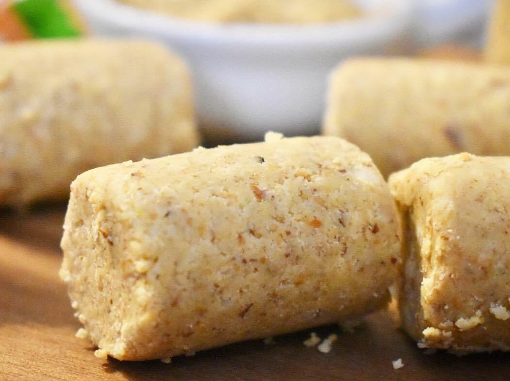 Close-up of TerraNut cold-pressed snack bites on a wooden surface with a bowl of crushed nuts in the background.
