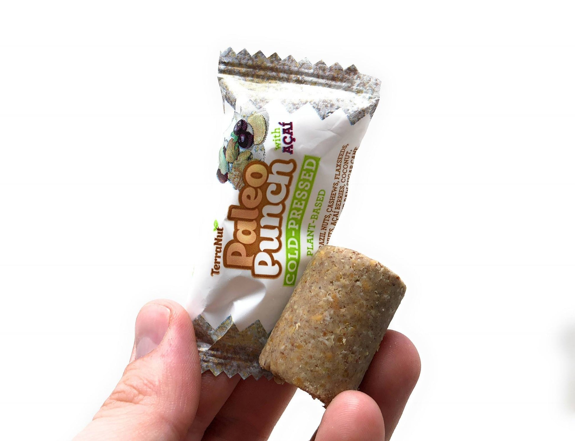 A hand holding a TerraNut Paleo Punch with Acai bar and a freshly made cold-pressed nut cylinder