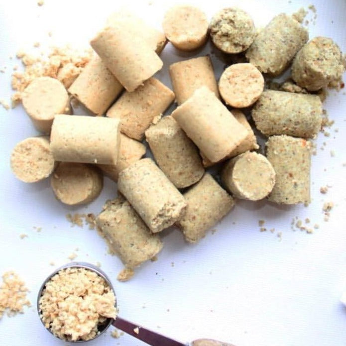TerraNut cold-pressed snack bites scattered on a white surface with crumbs and a small scoop of crushed nuts.